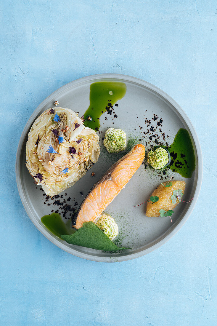 Baked salmon fillet and pike caviar with piece of cabbage on plate decorated with white sauce