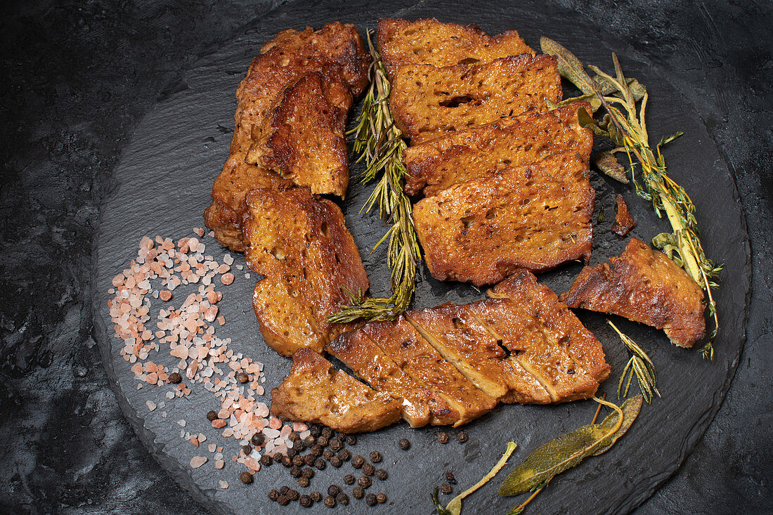 Gebratene Seitan-Steaks mit Kräutern und Gewürzen auf Schieferplatte