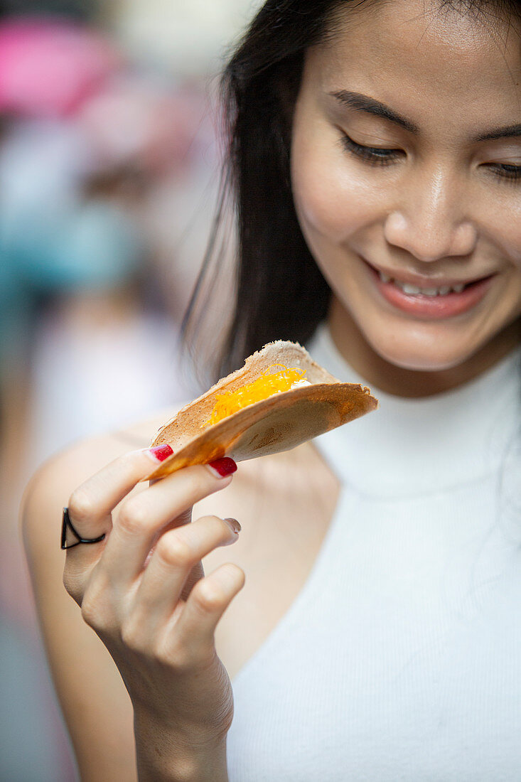 Young Asian woman eats Kanom Buang (crepe with cream filling and Foi Thong, Thailand)