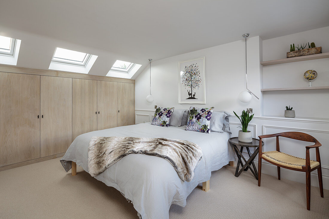Schlafzimmer in Weiß mit beigefarbener Einbauschrankwand unter Dachschräge mit Fenstern
