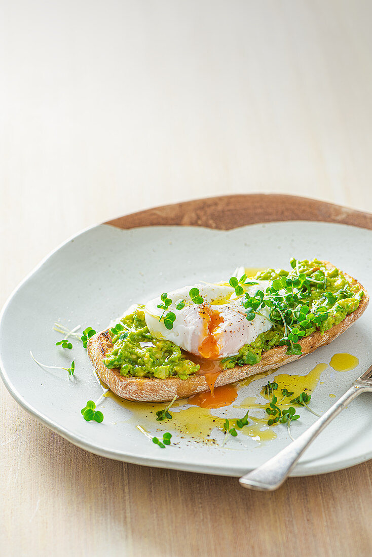 Pochiertes Ei auf Ciabatta-Toast mit zerdrückter Avocado, Kresse und Olivenöl