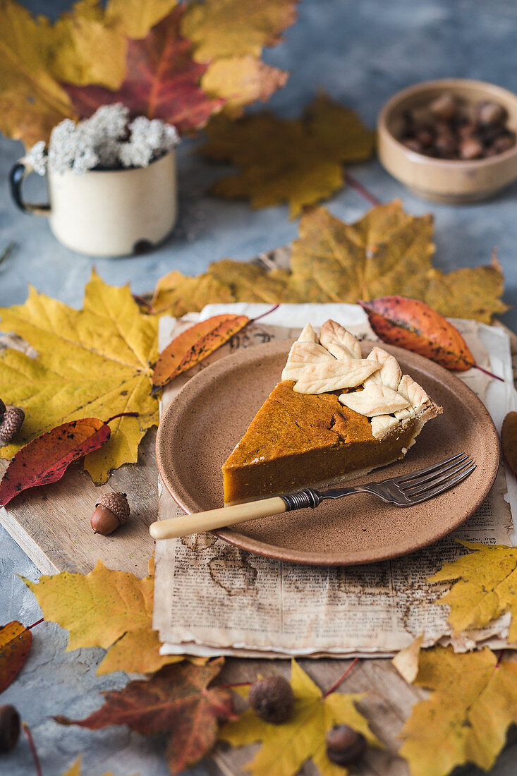 Ein Stück vegane Pumpkin Pie umgeben von Herbstlaub