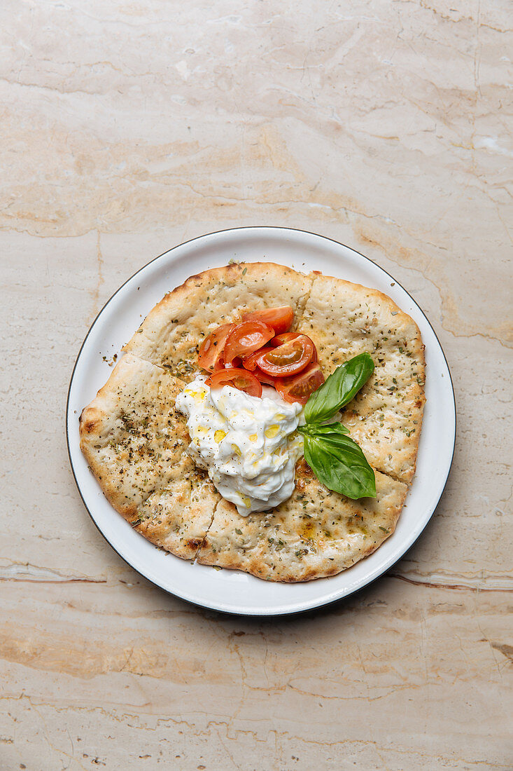 Baked golden dough served with creamy sauce slices of tomato and basil leaves