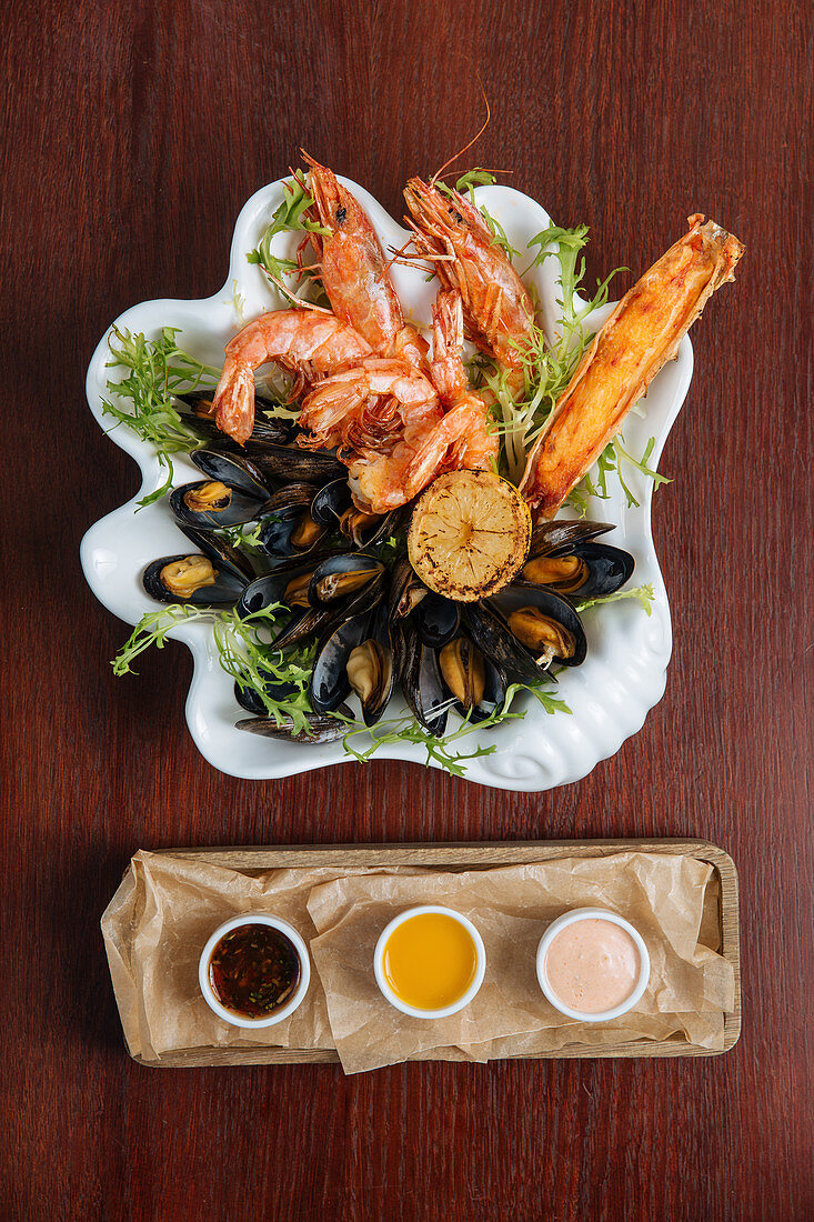 Grilled prawns and mussels with greens on plate with three sauces on side