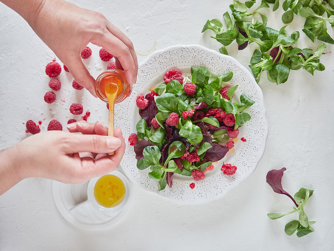 Person putting raspberry juice in fruit salad