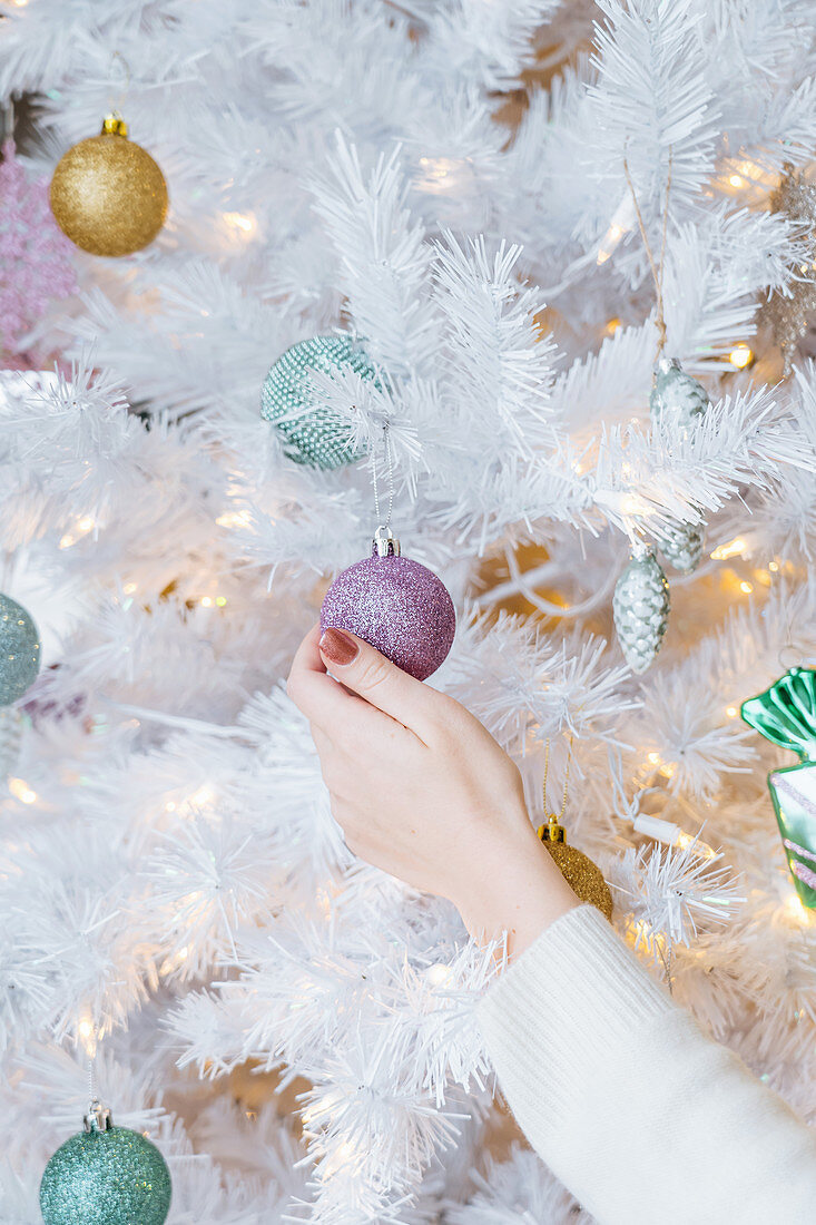 Person decorating artificial white Christmas tree with baubles