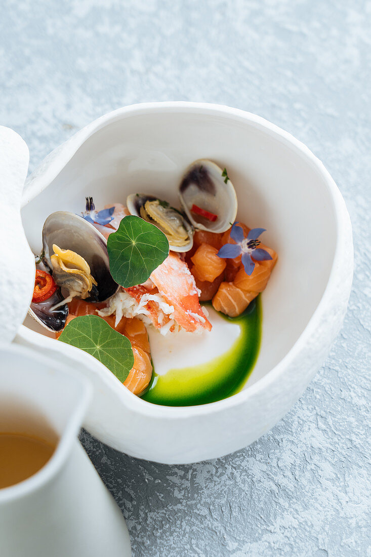 Seafood soup with salmon and clams decorated with flowers in bowl