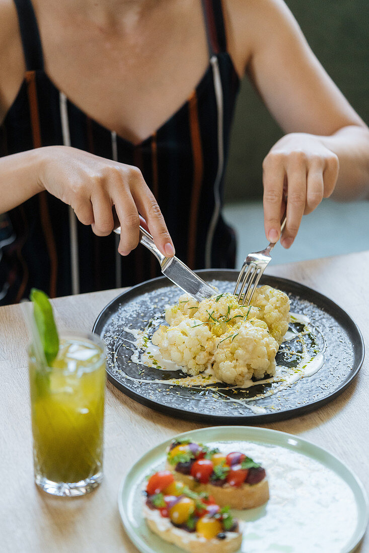 Woman cutting cauliflower in sauce at table with sandwiches and fresh lemonade