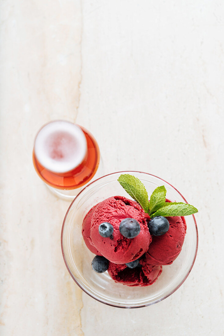 Purple scoops of ice cream in glass bowl with fresh blueberry and mint