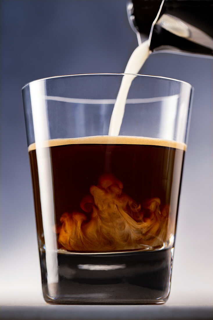 Milk is poured into a glass with espresso