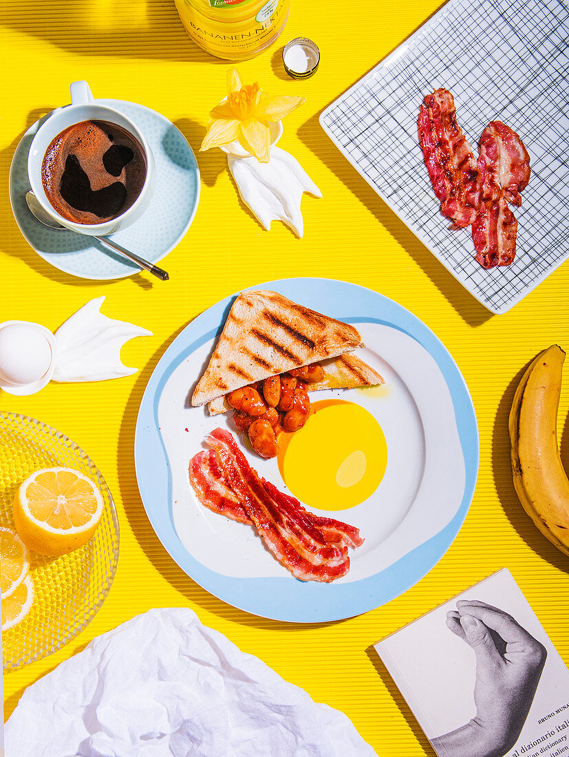 Breakfast with toast, baked beans and bacon on a plate with a fried egg motif