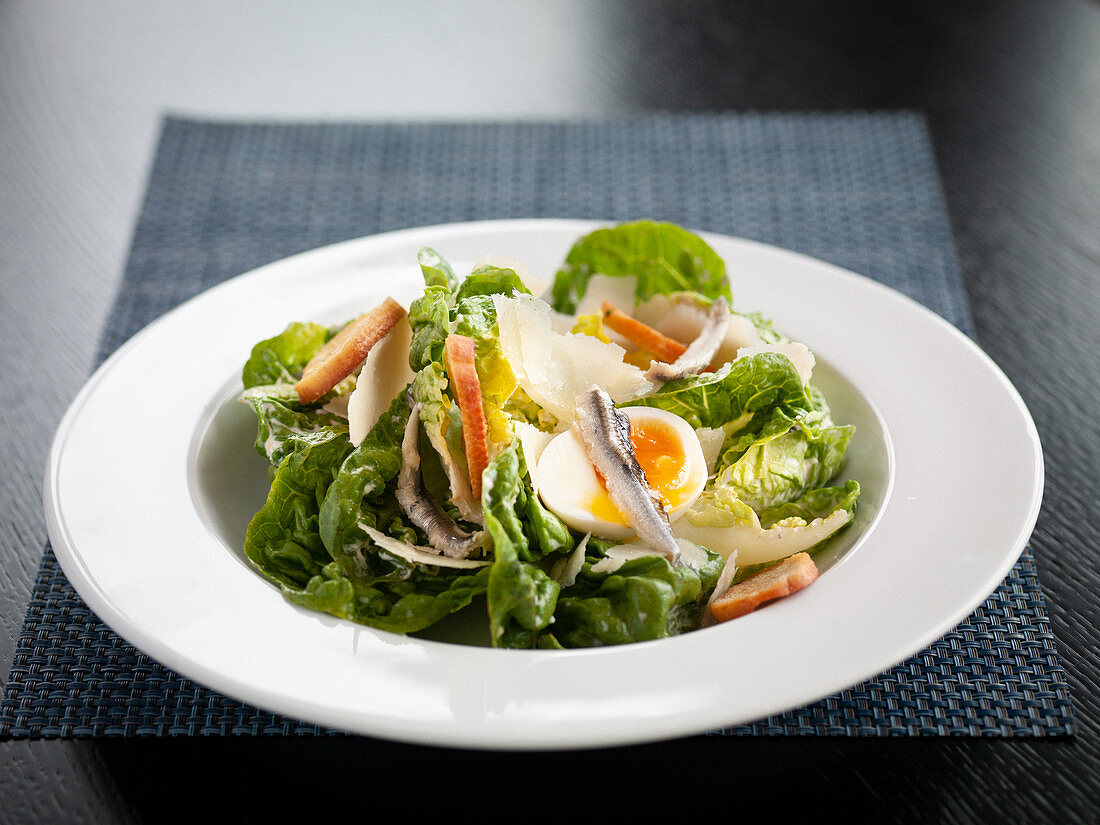 Caesar Salad mit Sardellen, gekochtem Ei, Brotchips und Parmesan