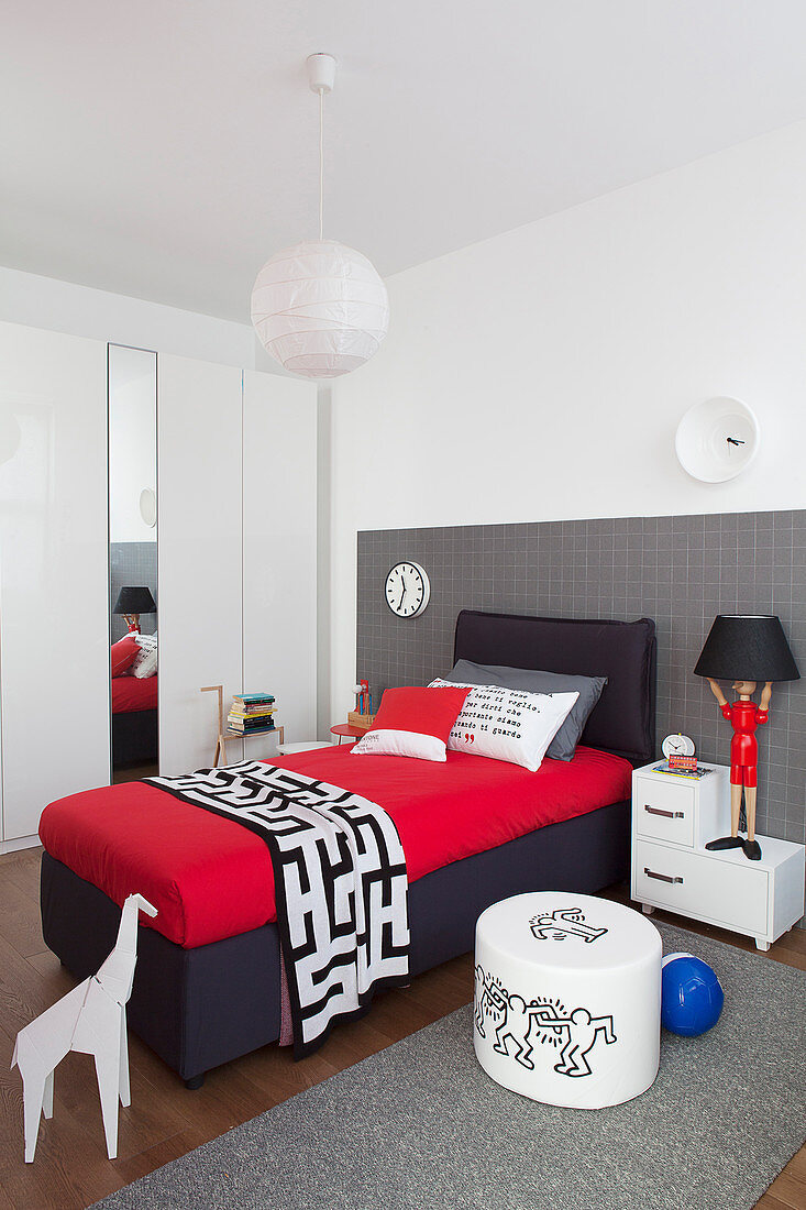 Box spring bed in black and red against grey checked wall in boy's bedroom