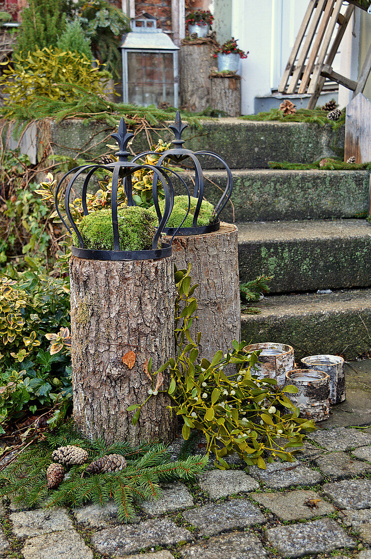 Moss and iron crowns on tree stumps, branch of mistletoe and candle lanterns next to steps