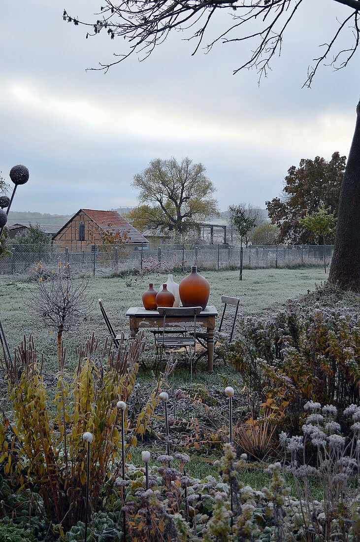 Late autumn in rustic garden: table and chairs with demijohns on table