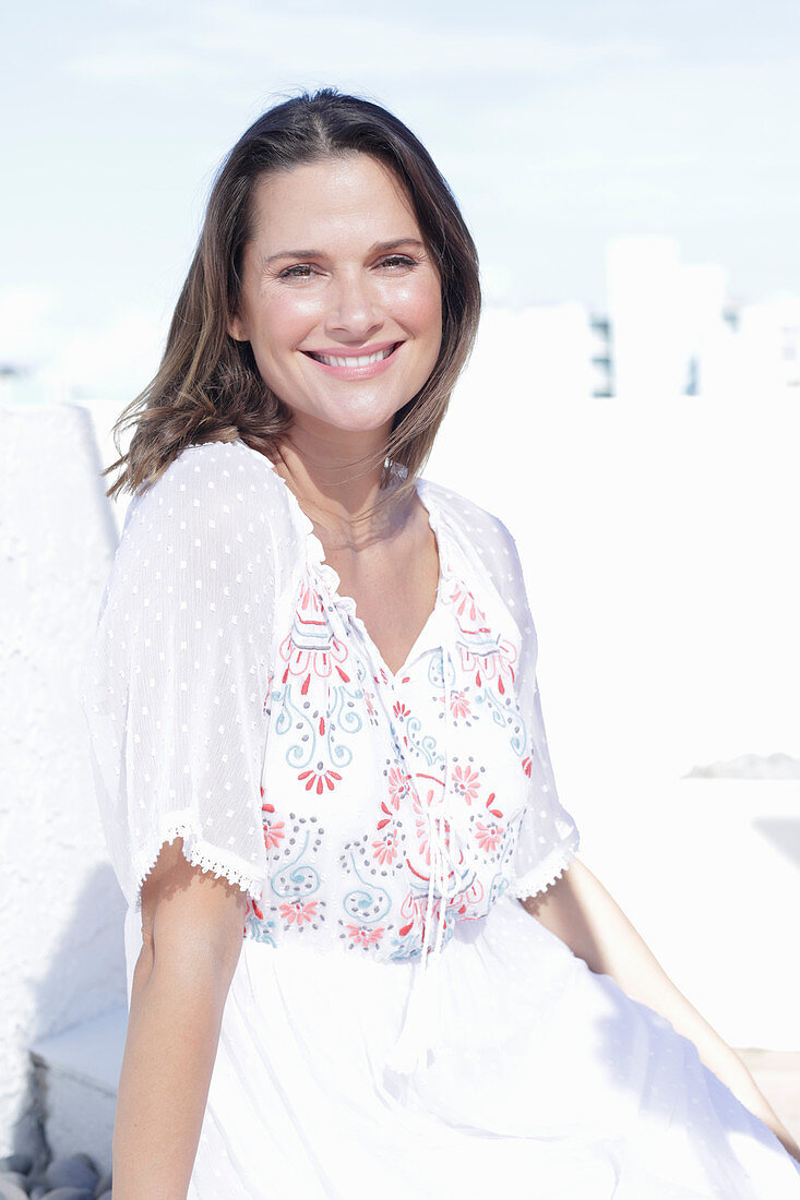 A long-haired woman wearing a white summer dress with colourful embroidery detail