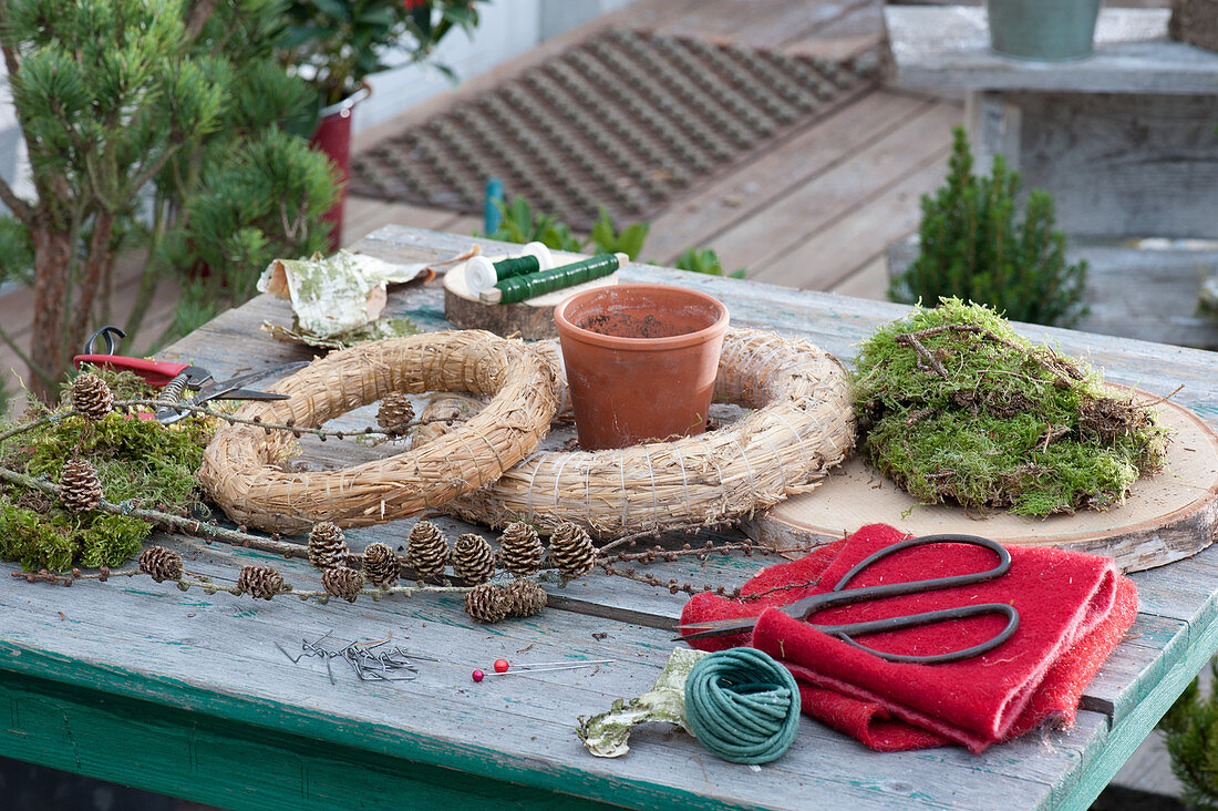 Ingredients for a homemade moss wreath cake with a candle: straw, moss, felt, wooden disc, scissors, larch twig, clay pot and winding wire
