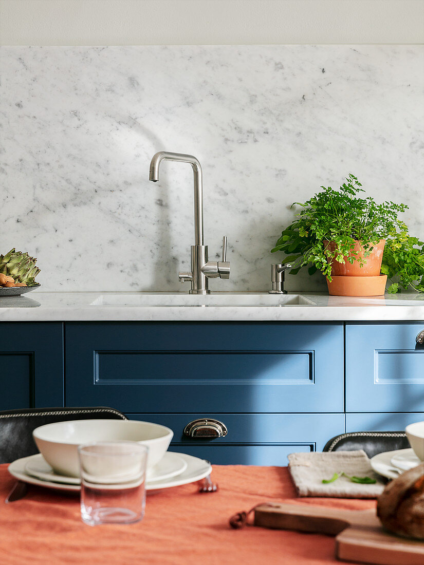 Blick vom gedeckten Esstisch auf die blaue Küchenzeile mit Spüle