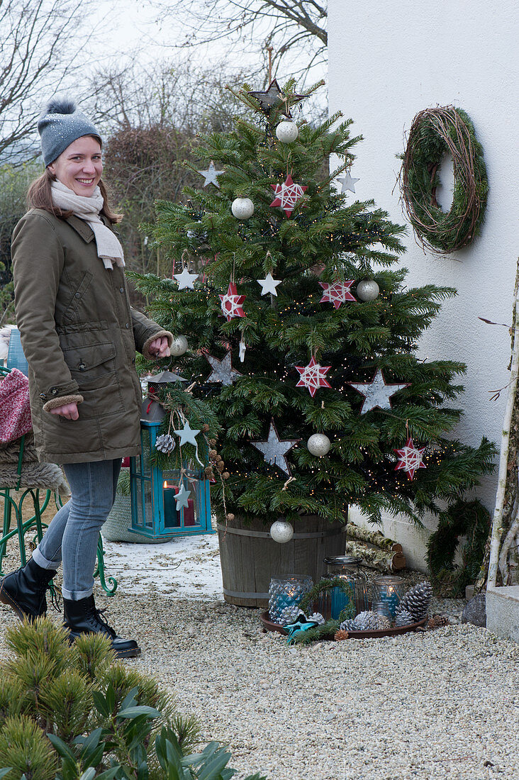 Nordmann fir decorated with stars and balls, woman brings a lantern