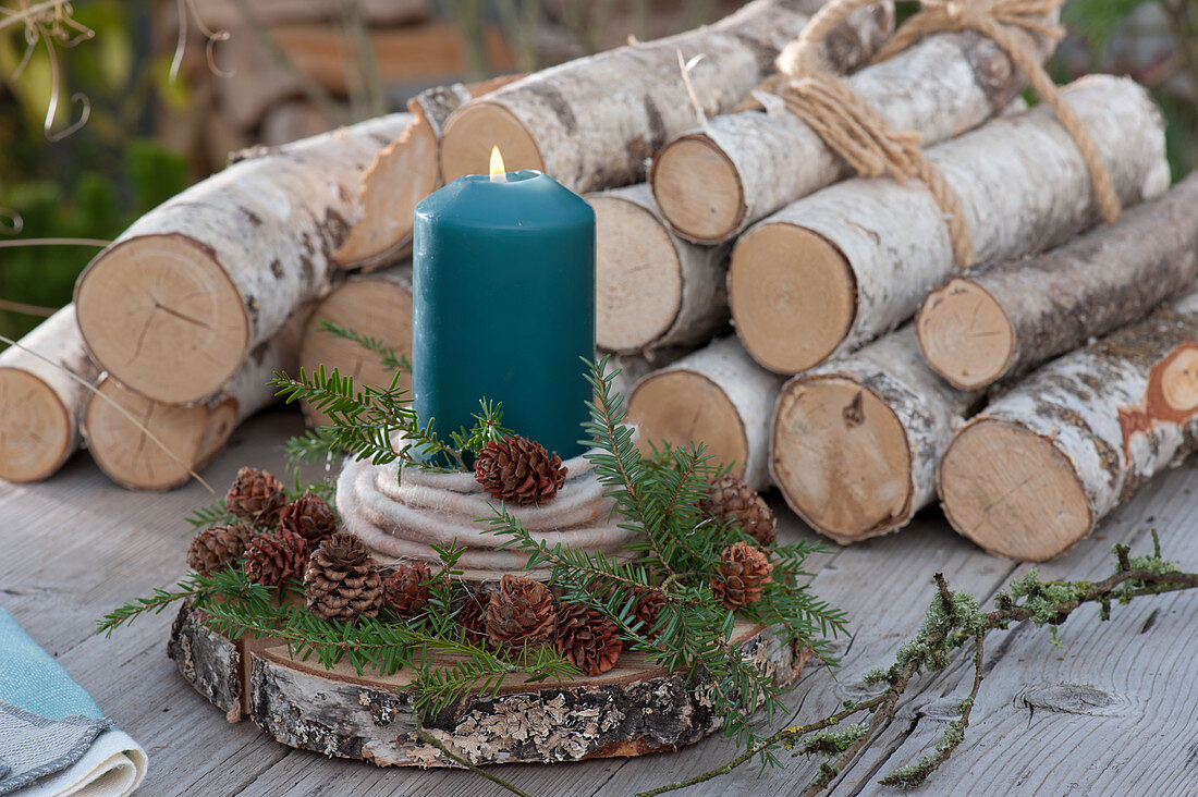 Candle with woolen cord and twigs with cones on a wooden disc