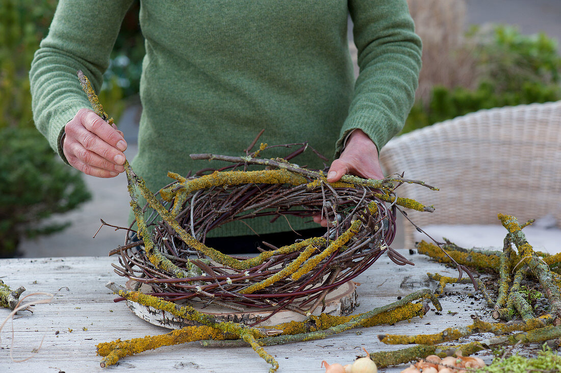 Snowdrops in a wreath of branches: woman winds a wreath made of lichen-covered branches, birch and willow