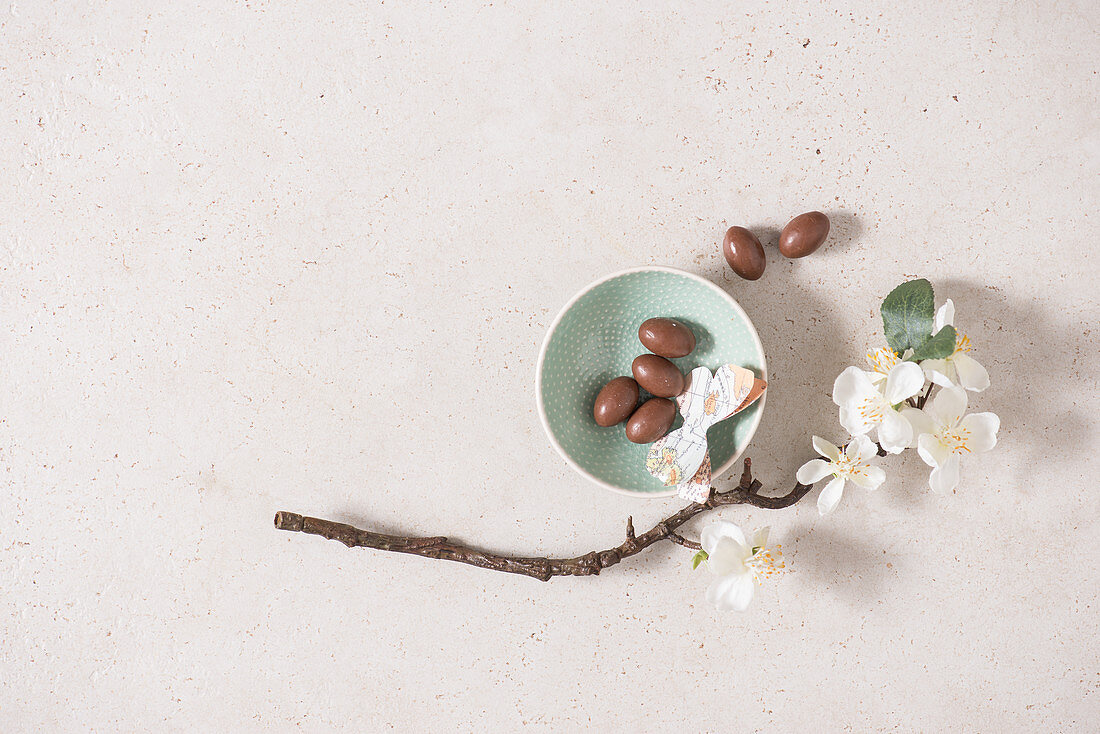 Chocolate eggs in a bowl decorated with paper butterflies and a sprig of blossom