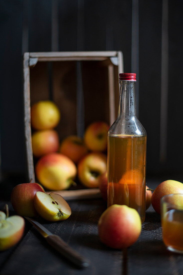 Eine Flasche Cidre, im Hintergrund Holzkiste mit Äpfeln