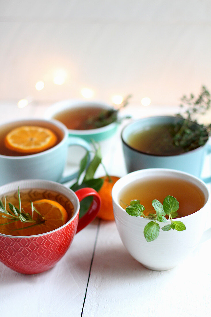 Teetassen mit verschiedenen Kräutern und Orangenscheiben