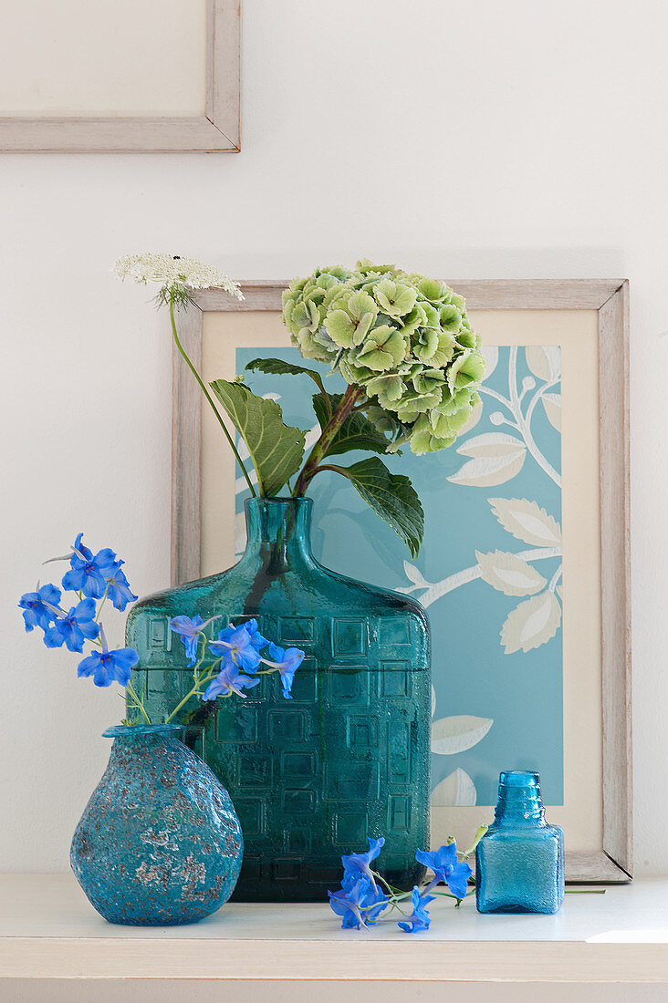 Blaßgrüne Hortensie in Vintage Glasvase, Rittersporn in türkisblauer Vase