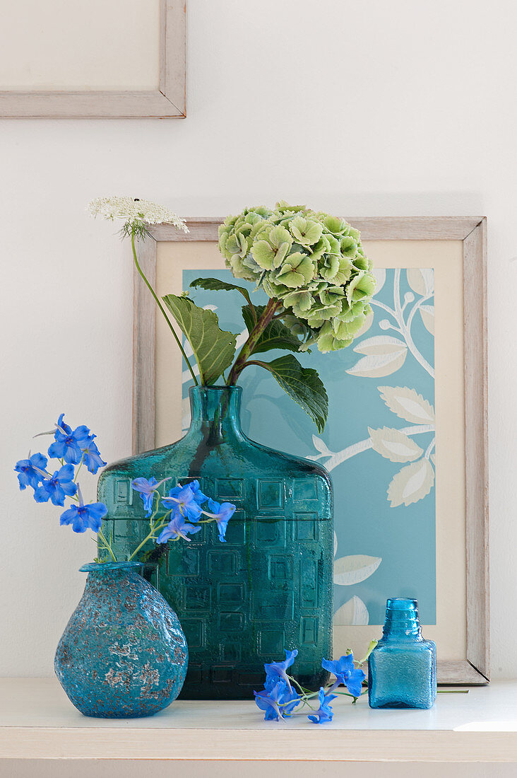 Pale green hydrangea in vintage glass vase and delphinium in turquoise vase