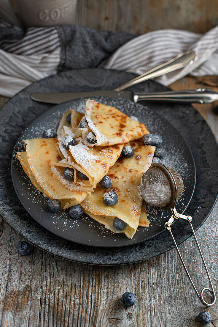 Crepes with blueberries, honey and icing sugar for breakfast