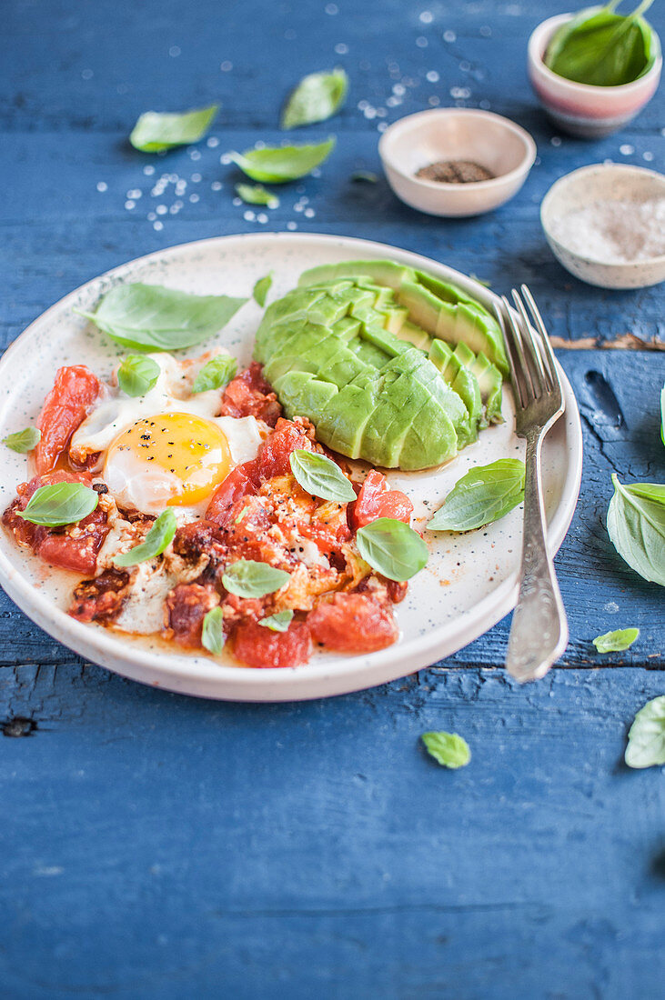 Shakshouka (in Tomatensauce gekochtes Ei) mit Avocado und frischem Basilikum