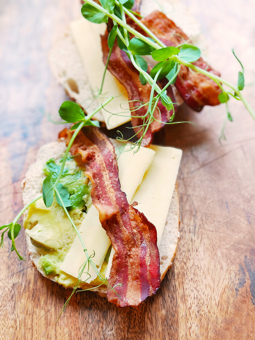A roll topped with avocado, bacon, cheese and pea sprouts