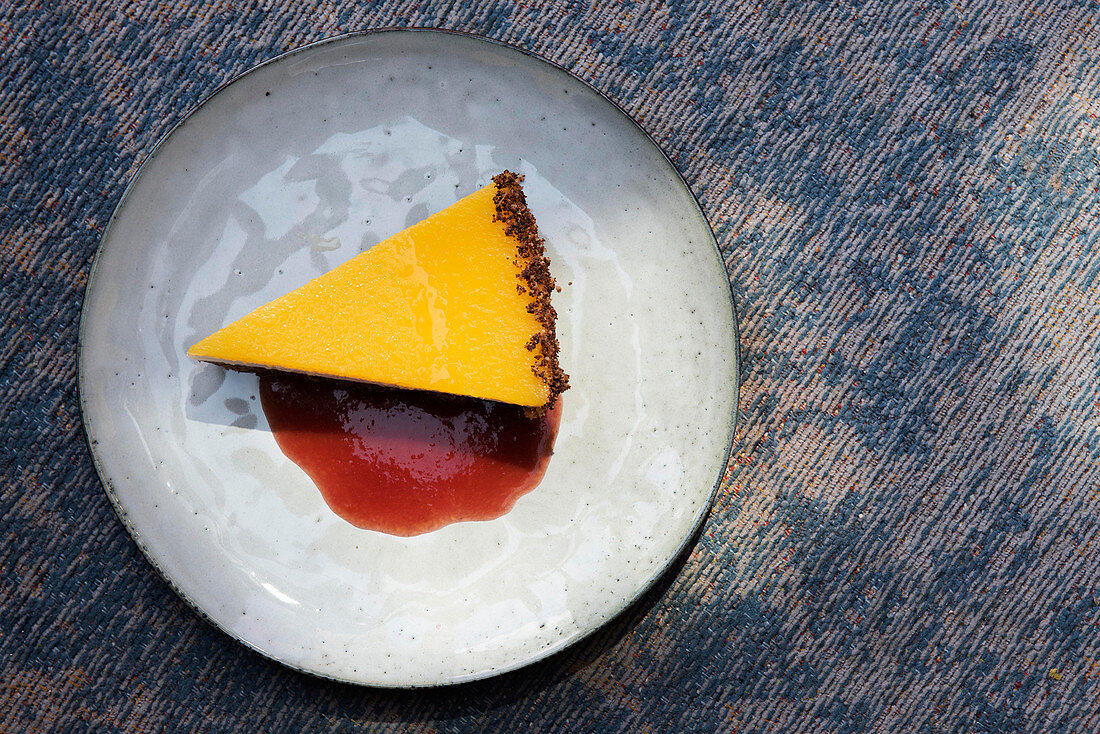 A slice of mango tart with yoghurt cream, a biscuit base and berry sauce