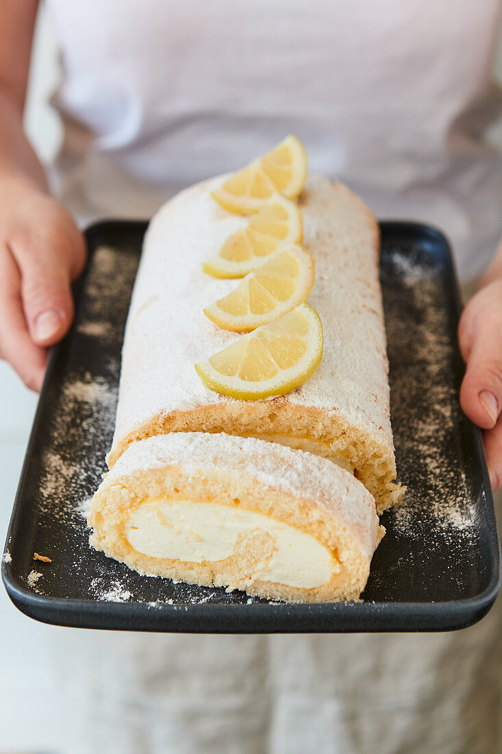 A woman holding a lemon Swiss roll on a tray