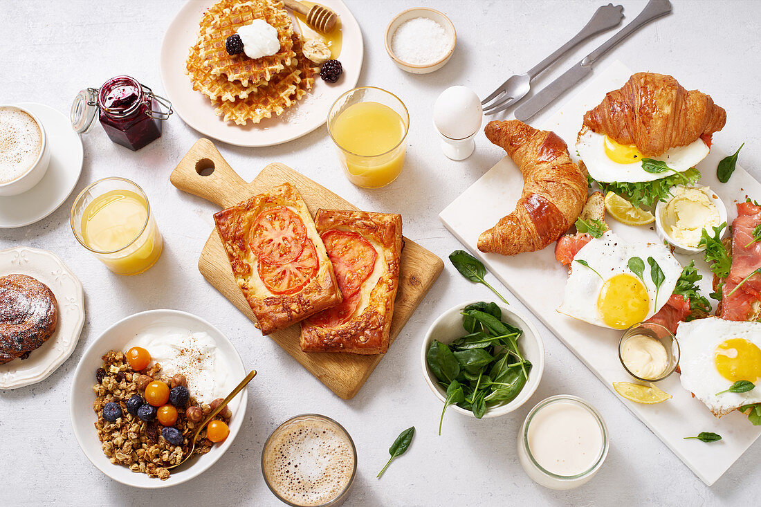 Gesundes Sonntagsfrühstück mit Croissants, Waffeln, Eiern, Müsli und Sandwiches