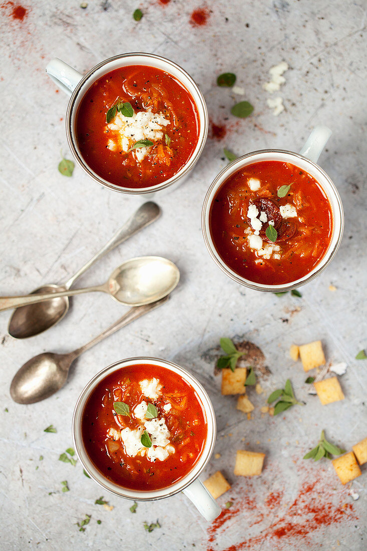 Enamel cups with smoky tomato soup topped with feta and herbs