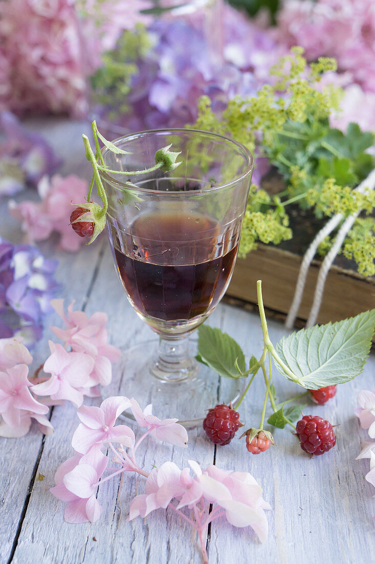 Ein Glas Himbeerlikör mit Hortensien und Himbeeren