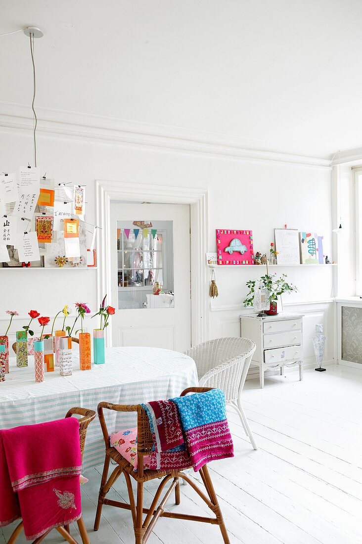 Wicker chairs around table in white dining room with brightly coloured accents