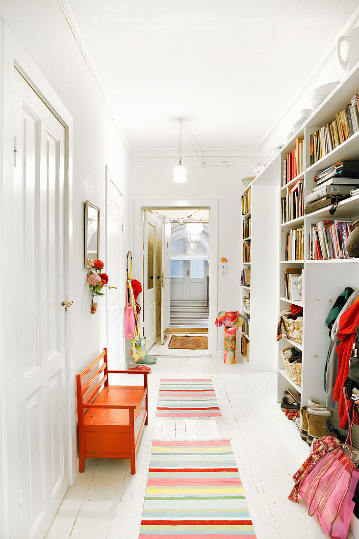 Striped, multi-coloured runners and orange bench in white hallway