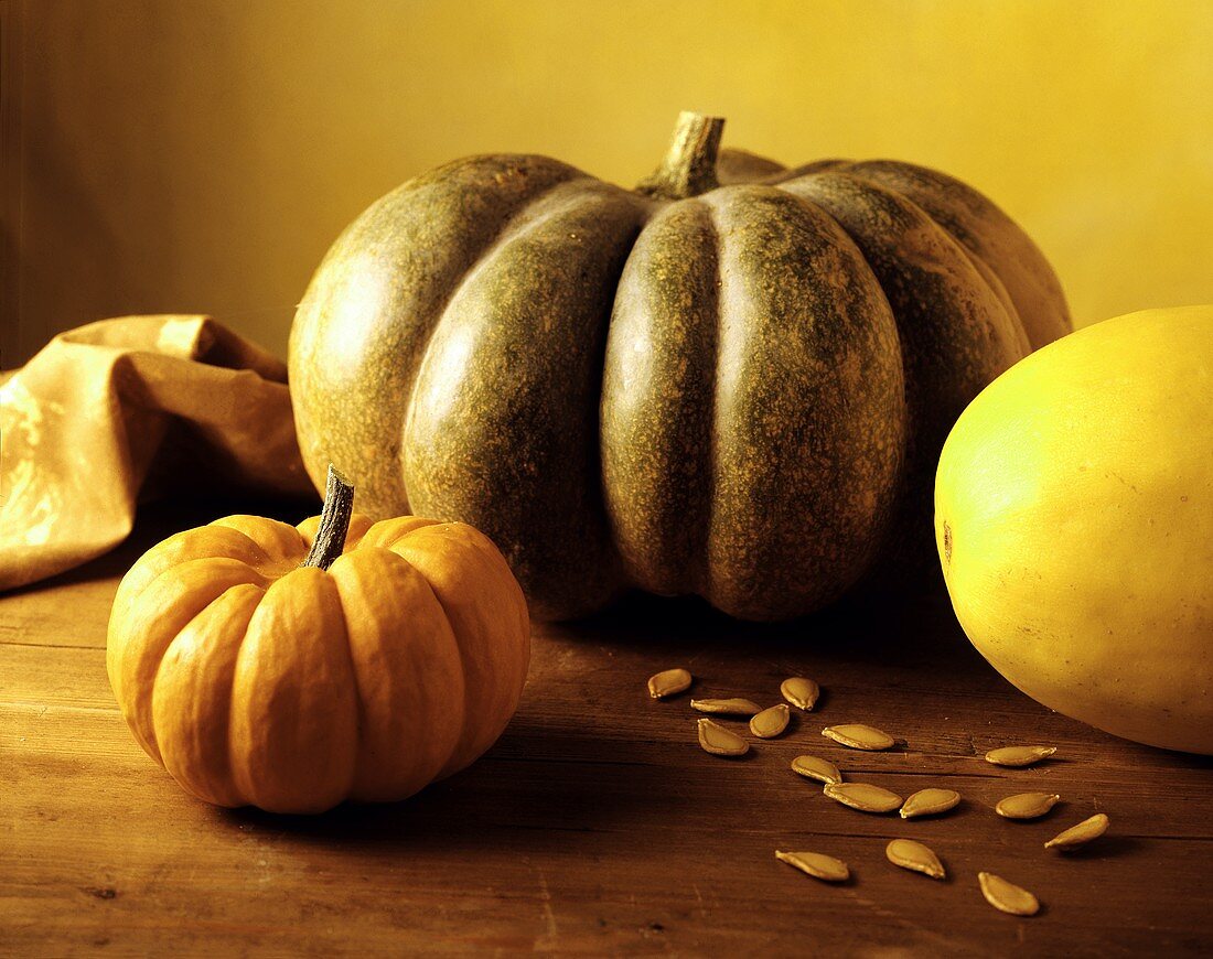 Three different pumpkins & pumpkin seeds on wooden table