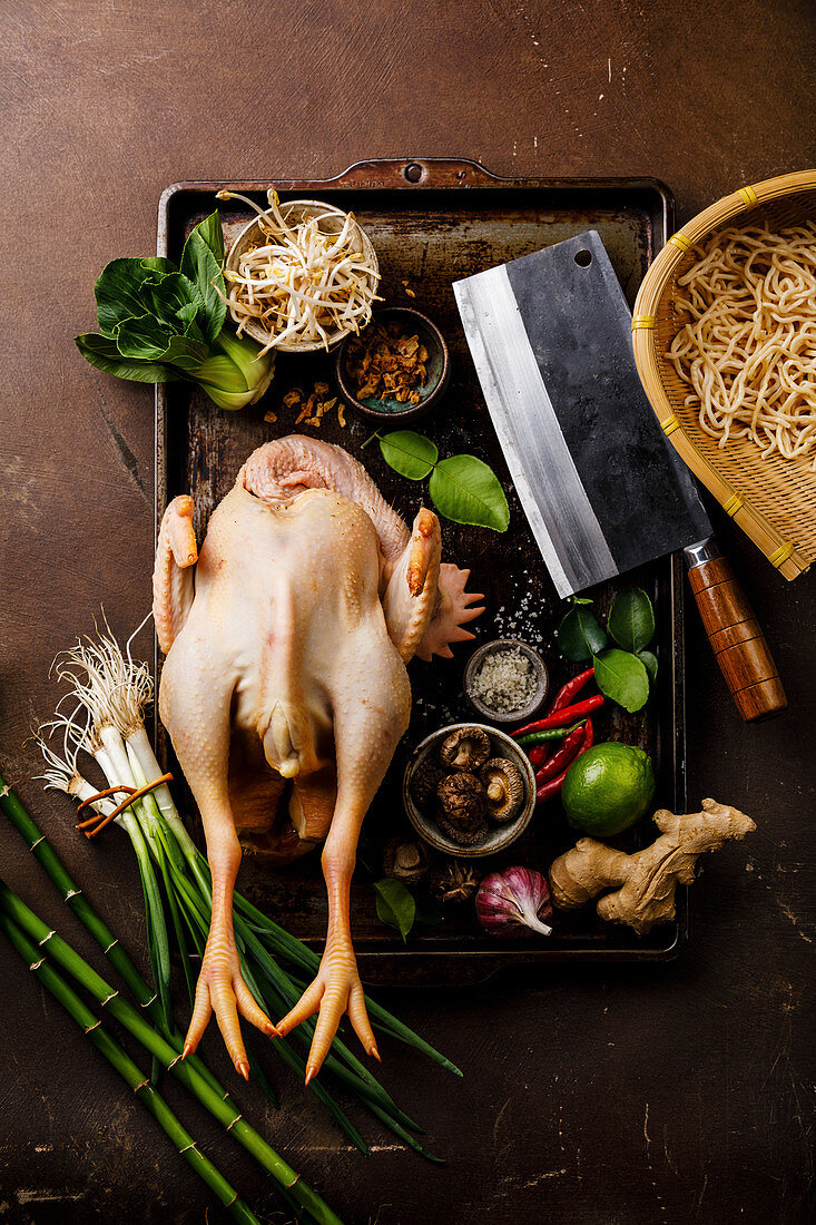 Rohes Huhn mit Küchenbeil und verschiedenen asiatischen Zutaten