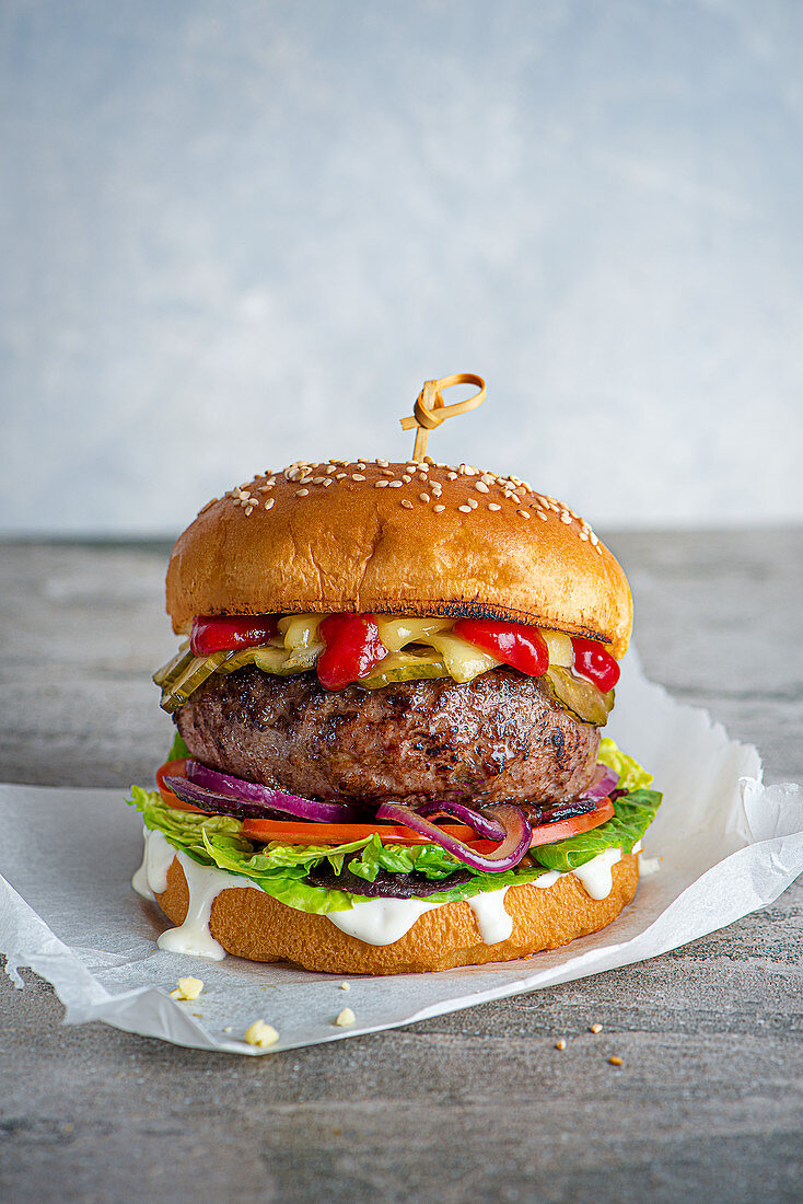 Cheeseburger mit Essiggurke, Tomaten, Zwiebeln, Salat, Mayo und Ketchup