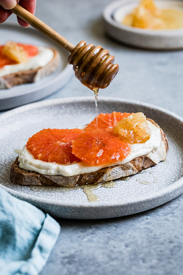 Honey orange ricotta toast on a ceramic plate. Vanilla-laced whipped ricotta gets swirled on toast and topped with orange slices and a drizzle of honey