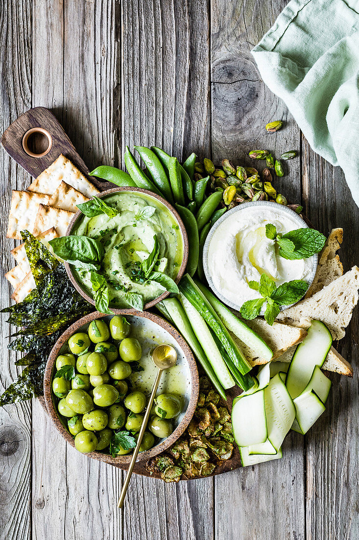 A dipping board with olives, cucumber, dips, bread, crackers and nuts.