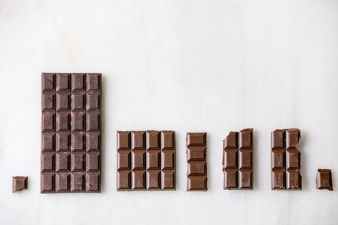 Dark and milk chocolate bar whole and chopped in row over white marble background. Flat lay, space