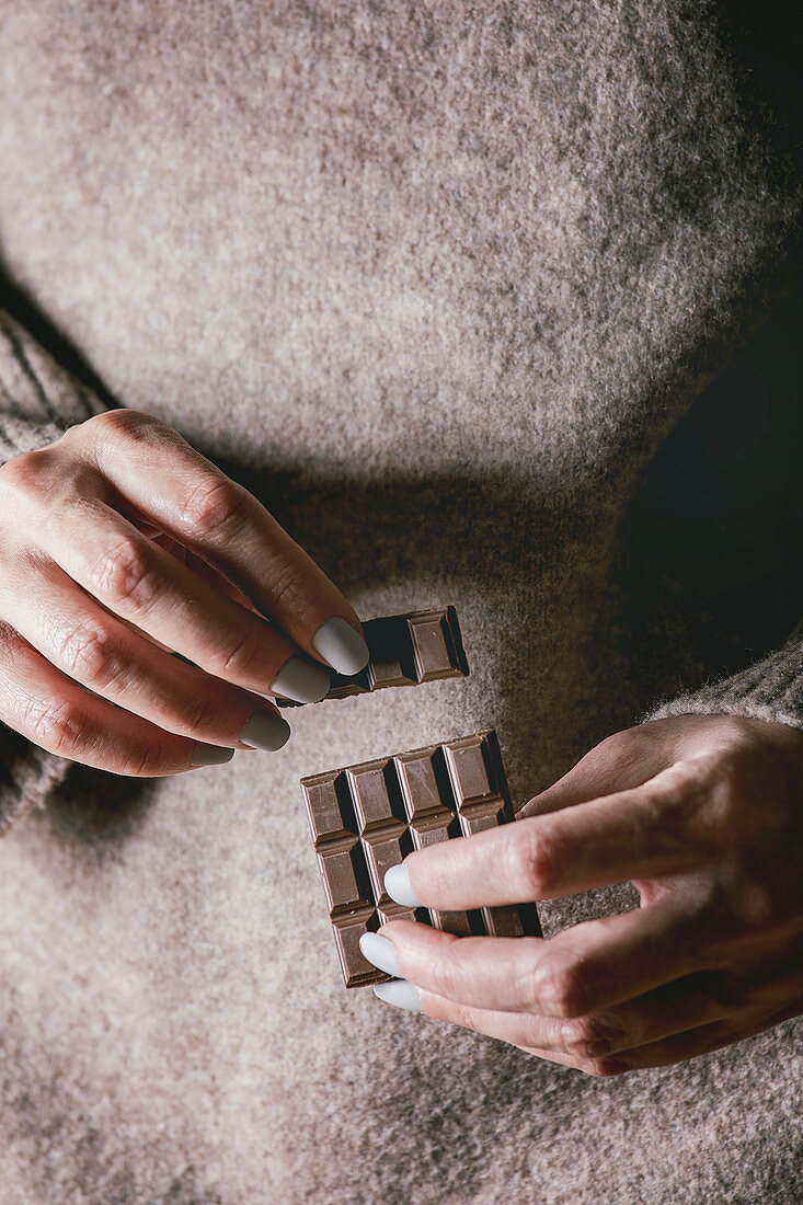 Woman beige sweater hold in hands broken dark chocolate bar