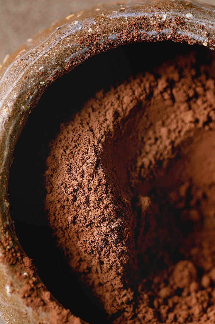 Cocoa powder in ceramic bowl with cocoa beans over brown texture background. Flat lay, close up