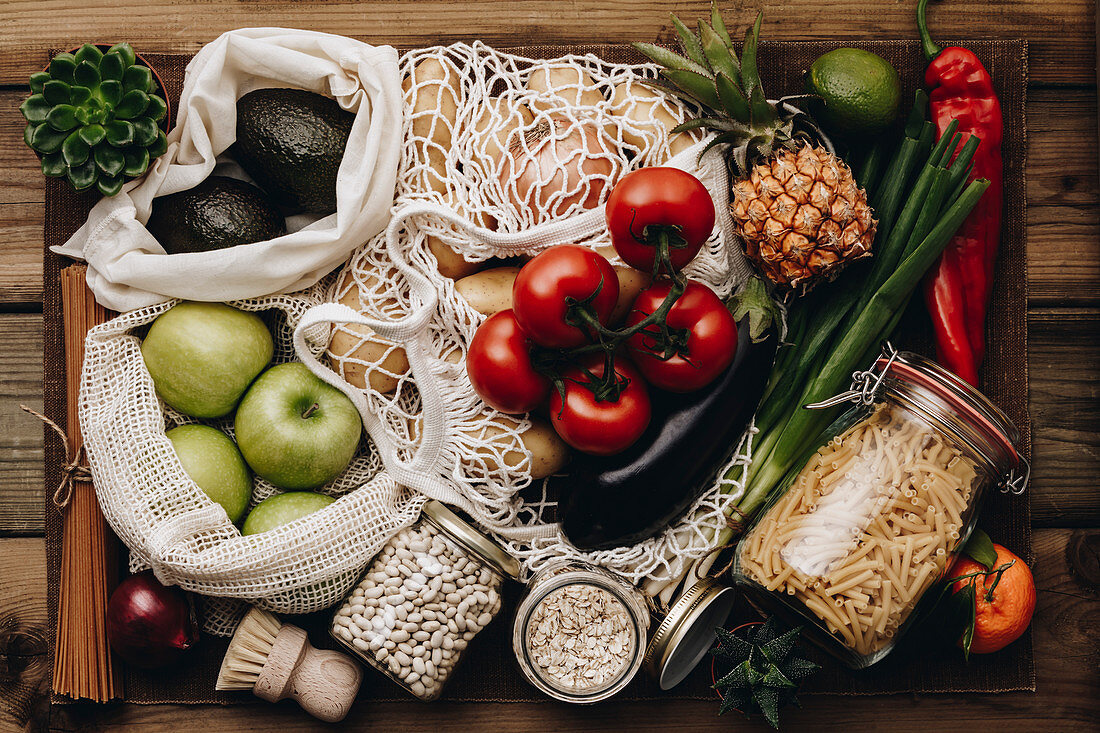 Zero waste food shopping. Fruit and vegetables in cotton bags, pasta, cereals and legumes in glass jars, herbs and spices on wooden background