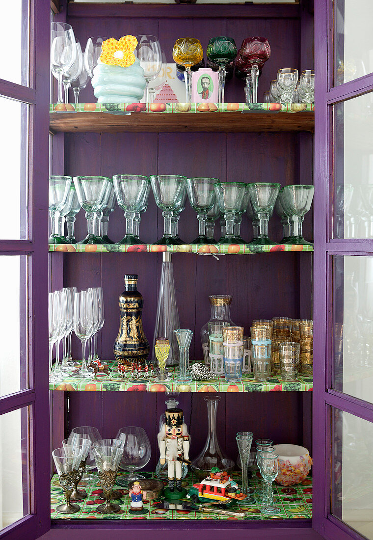 Old glasses in purple, glass-fronted cabinet with multi-coloured shelves